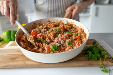 Wall Mural - Woman serving a healthy dinner with tuna, rice and vegetable in a skillet on kitchen background