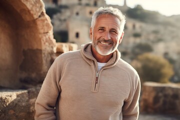 Wall Mural - Portrait of a cheerful man in his 60s dressed in a comfy fleece pullover over backdrop of ancient ruins