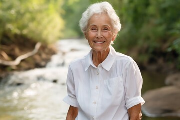 Wall Mural - Portrait of a smiling elderly woman in her 90s wearing a classic white shirt over tranquil forest stream