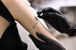 © New Africa - Professional artist in gloves applying cream onto woman's arm with fresh tattoo in salon, closeup