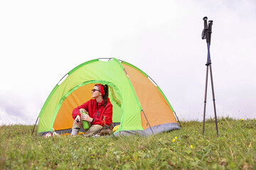 Wall Mural - Young woman with thermo bottle sitting in camping tent on green grass outdoors