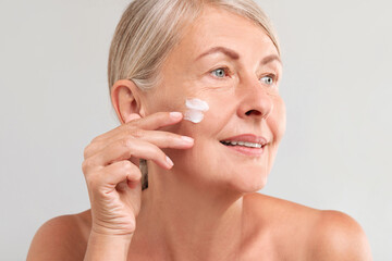 Wall Mural - Senior woman with face cream on light background