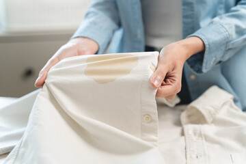 Wall Mural - Housewife, asian young woman hand in holding shirt, showing making stain, spot dirty or smudge on clothes, dirt stains for cleaning before washing, making household working at home. Laundry and maid.