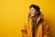 © Markus Schröder - Portrait of a joyful asian man in his 20s wearing a warm parka in soft yellow background