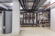 © alhim - Industrial piping and control systems in a modern building utility room featuring valves and a cylindrical unit