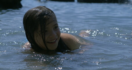 Smiling girl swimming in lake, captured in slow-motion at 800 fps, enjoying summer day, playful and joyful expression, water droplets