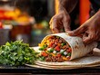 © JAKE STUDIO - A hands-on preparation of a vibrant burrito, filled with meat and fresh vegetables, alongside a bunch of chopped cilantro.