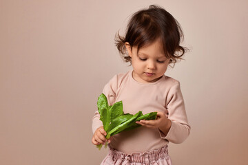 cute child girl holding fresh green salad on beige background. healthy baby food.