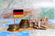© Alina - German flag near coins and parcels on a world map. World trade, export and import of goods around the world