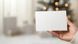 © Bonsales - Woman is holding blank white card, blurred christmas tree with lights on background, space for mockup
