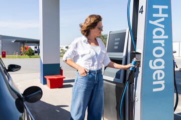 Woman holds a hydrogen fueling nozzle on a hydrogen filling station. Refueling car with hydrogen fuel