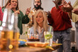 © PintoArt - Group of diverse people celebrating birthday with senior woman blowing candles on cake at home party