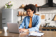 © wpadington - Portrait of smiling African American man wearing casual clothes working from home using laptop computer while sitting in the contemporary light colored loft interior kitchen