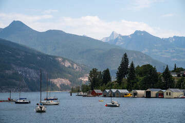 Tranquil lake view with colorful boats and wooden cabins against a backdrop of mountains on a sunny day