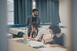© qunica.com - Students are deeply engaged in studying at their desks in a classroom setting. A teacher stands by, overseeing their progress. This setting reflects a focused and collaborative educational environment