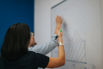 Two individuals are actively collaborating, drawing diagrams on a whiteboard. The scene conveys teamwork, creativity, and brainstorming in a professional or educational environment focusing on data