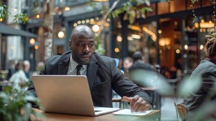 African American Black businessman wearing a suit working on laptop or waiting for a meeting in a modern cafe