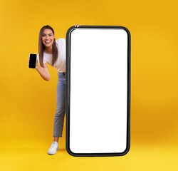 Wall Mural - full body length of cheerful woman peeking out standing behind big smartphone with white blank scree