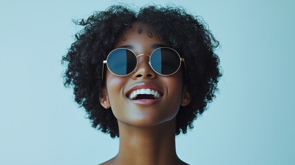 Smiling woman with curly hair wearing stylish sunglasses against a light blue background indoors during a bright day