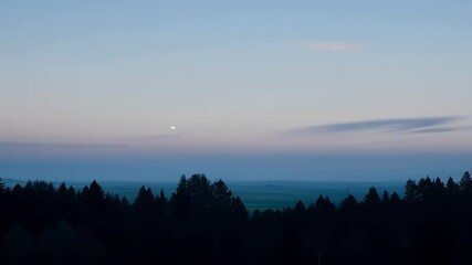 Wall Mural - Serene twilight sky with shades of blue. Purple. And pink. A pale moon shining over a mist filled valley. A dark forest standing tall in the evening light