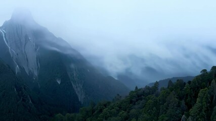 Wall Mural - mist is swirling around a tall mountain peak, waterfalls cascade down the side of the mountain into 