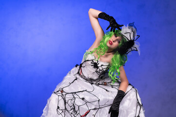 Girl in scary wedding dress with black web, green hair and head decorations. Scary Halloween bride costume. Halloween celebration. Dead bride costume