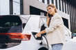 © anatoliycherkas - Young Woman Charging Electric Car While Talking on Phone