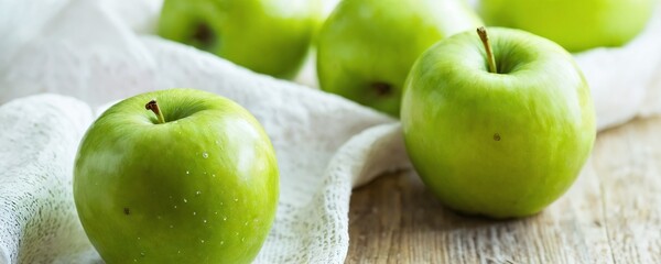 Wall Mural - Fresh green apples arranged on a wooden table with a light cloth in a bright kitchen setting