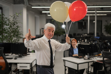 Portrait of a cheerful mature business man holding balloons in the office.