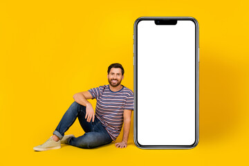 Poster - Photo portrait of young guy promoter sitting floor near empty space smartphone display ad promo on yellow color background