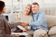 © Prostock-studio - Sealing A Deal. Happy elderly couple sitting on couch and shaking hands with young female financial advisor