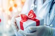 © Konstiantyn Zapylaie - Doctor holding a gift box with red ribbon against bokeh lights background