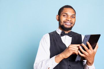 professional bellhop browses hotel website on a tablet in studio, wearing suit and tie while he chec