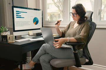 A woman is sitting at a desk with a laptop and a monitor