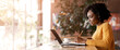 © Prostock-studio - Young black lady taking notes in front of laptop, looking for job online at cafe, empty space
