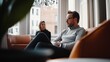 © LifeMedia - An engaged middle-aged man with glasses and beard, seated in a light-filled lounge, engaged in serious conversation, exuding thoughtfulness and quiet determination.