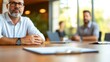 © LifeMedia - A man sits in a meeting room, wearing casual attire, with documents on the table. The blurred background captures a discussion among colleagues.