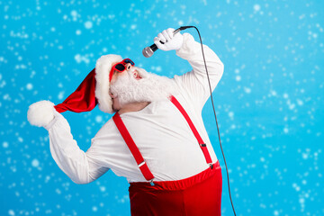 Wall Mural - Photo of old man grey beard hold mic open mouth sing song wear santa claus x-mas costume headwear sunglass suspenders white shirt gloves isolated blue color background