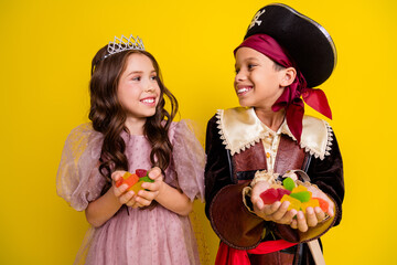 Canvas Print - Portrait of two kids halloween princess pirate costume hold candy look each other isolated on yellow color background