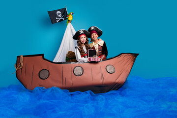 Poster - Full size photo of two small kids halloween pirate costume hug hold jewelry chest sail ship isolated on blue color background