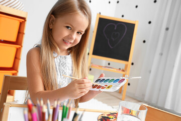 Cute little girl drawing with paints at home