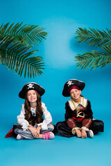 Canvas Print - Full size vertical photo of two small kids sit floor halloween pirate costume isolated on blue color background