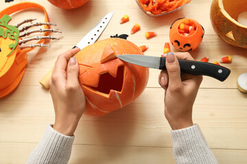 Wall Mural - Woman carving Halloween pumpkin at wooden table