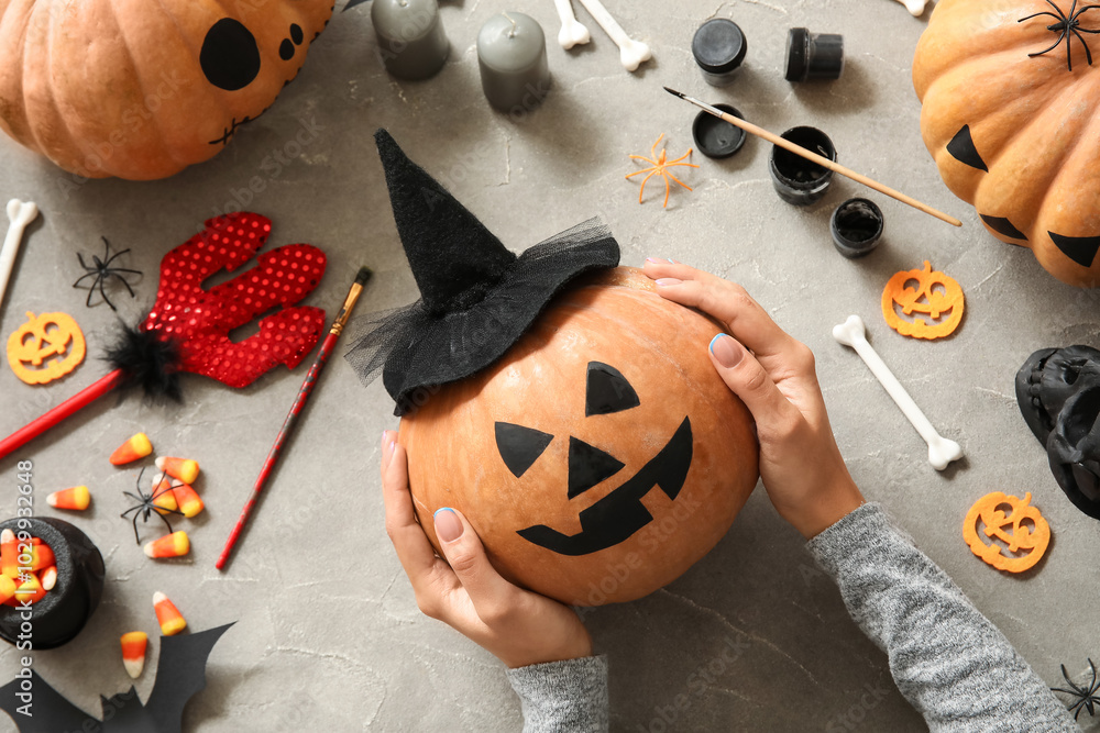 Woman with painted Halloween pumpkin at grey grunge table