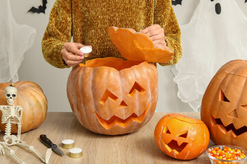 Sticker - Woman putting candle into carved Halloween pumpkin at wooden table