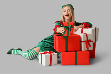 Wall Mural - Young woman in elf costume with Christmas gift boxes on white background