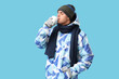 © Pixel-Shot - Young man in stylish puffer jacket and scarf with paper cup of coffee on blue background