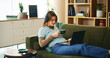© AzeemudDeen/peopleimages.com - Laptop, headphones and girl on sofa with coffee, comfort or listening to online webinar in home. Elearning, relax and student on couch with computer, podcast connection or music streaming in lounge
