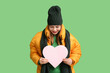 © Pixel-Shot - Beautiful young woman in warm winter clothes with paper heart on green background