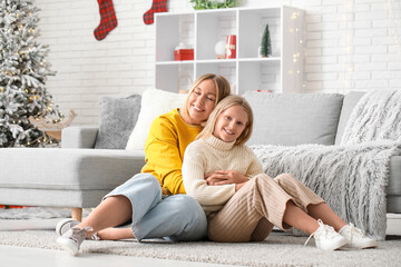 Beautiful woman and her cute daughter in stylish sweaters sitting on carpet at home